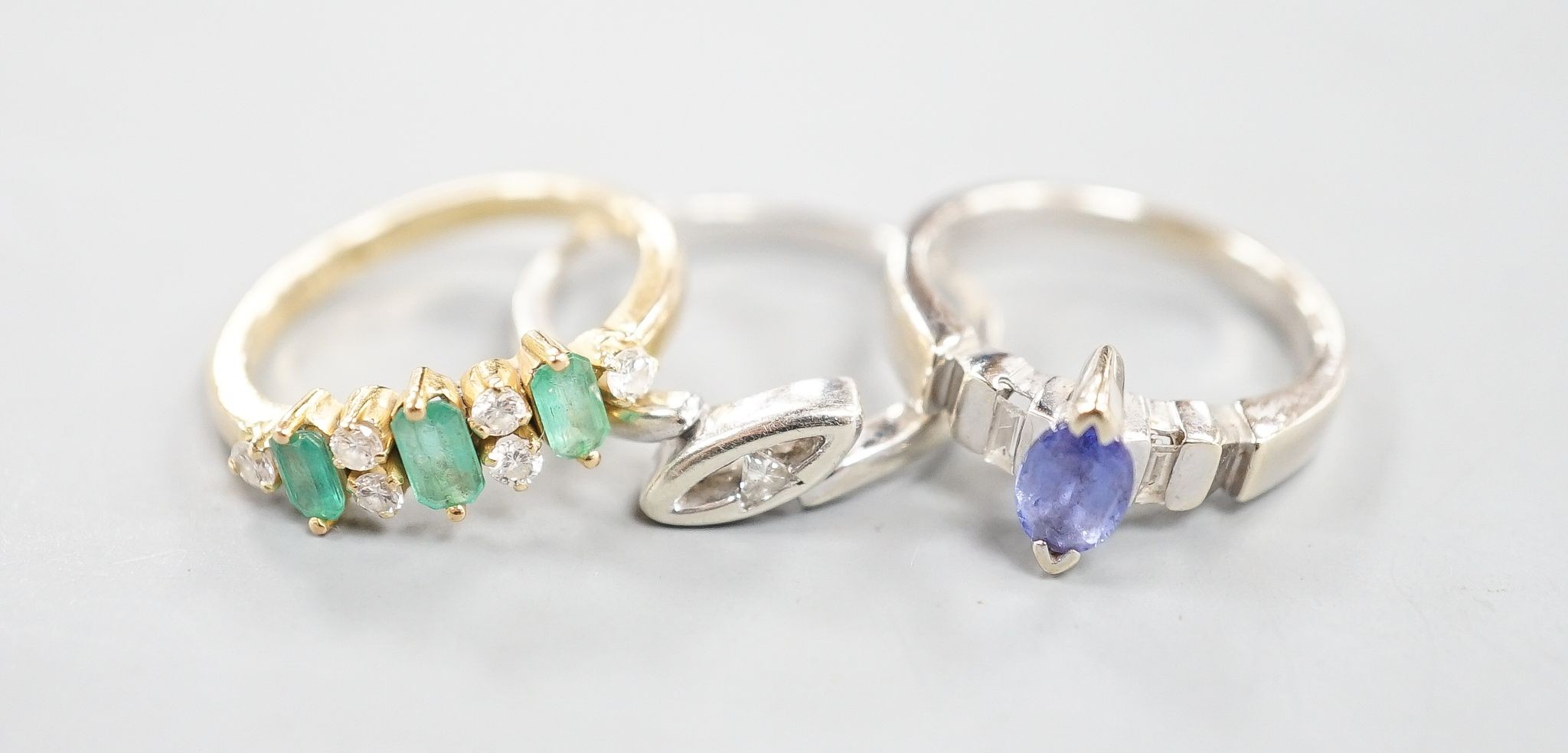 A 750 yellow metal, three stone emerald and six stone diamond chip set half hoop ring, size L, a 750 white metal and tanzanite ring, size K, gross 6.4 grams and a 9ct white gold and diamond chip set ring, gross 2.4 grams